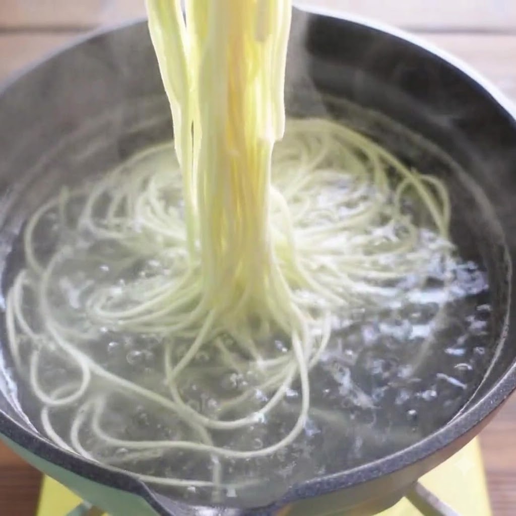Des baguettes soulevant des nouilles de ramen cuites hors de leau bouillante.