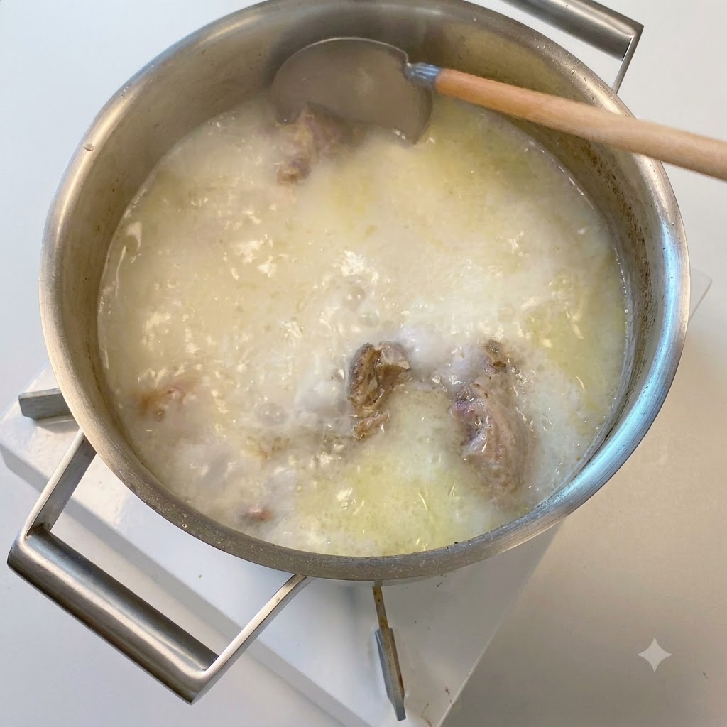 Une louche en bois plongeant dans une casserole de bouillon dos de porc frémissant, blanc opaque et laiteux.