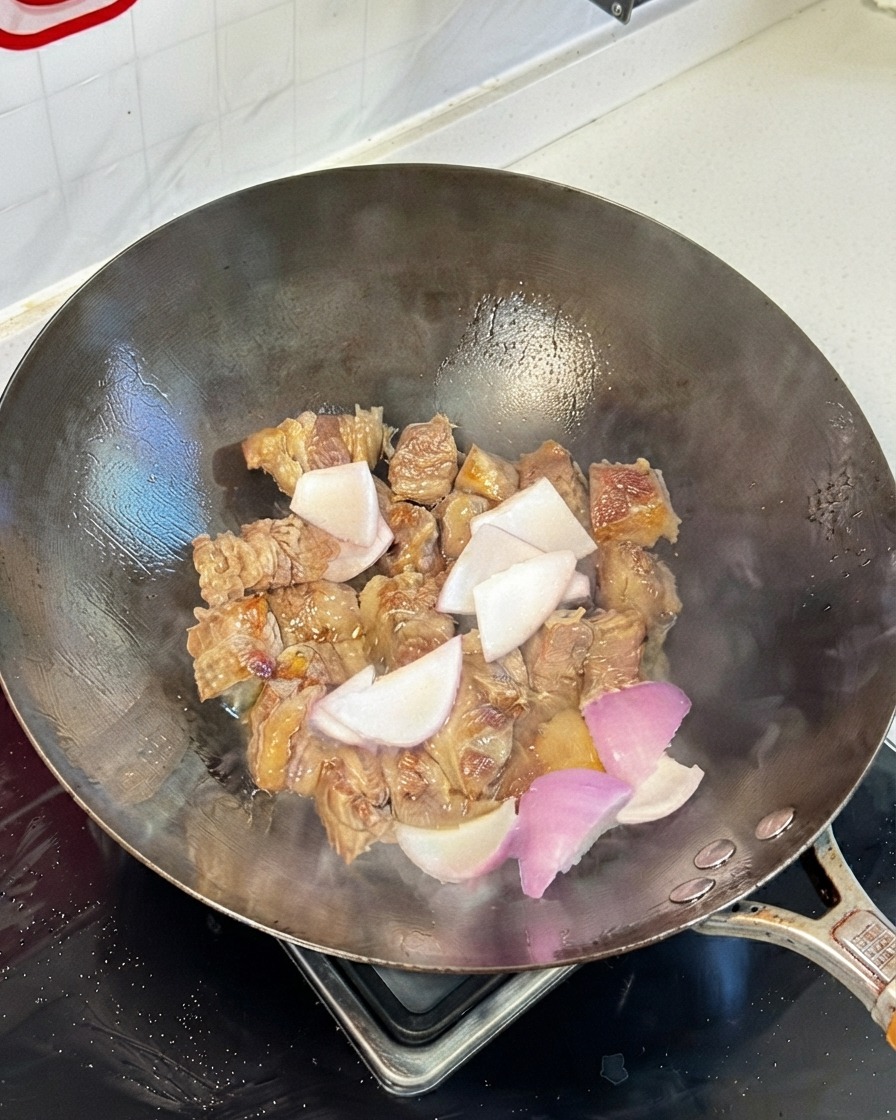 Morceaux de côtes de bœuf sautés dans un wok mélangés avec des morceaux doignon et des sauces soja.