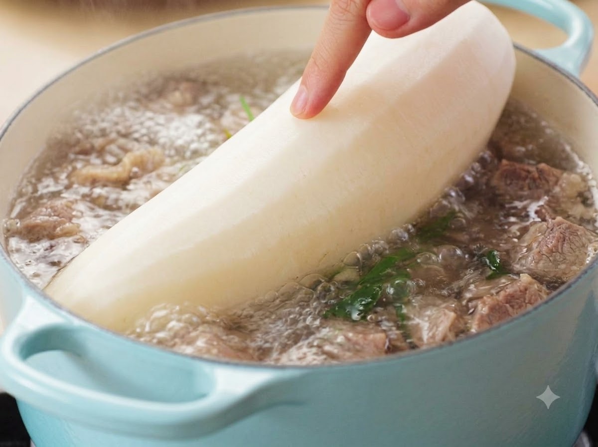 Une main guidant un grand radis blanc épluché dans une soupe de bœuf bouillante.