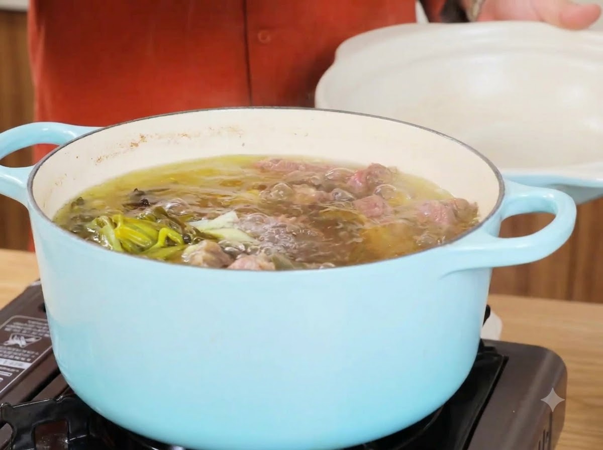 Une casserole de bouillon de bœuf frémissant après avoir retiré les ingrédients principaux, montrant un liquide clair et des oignons verts.