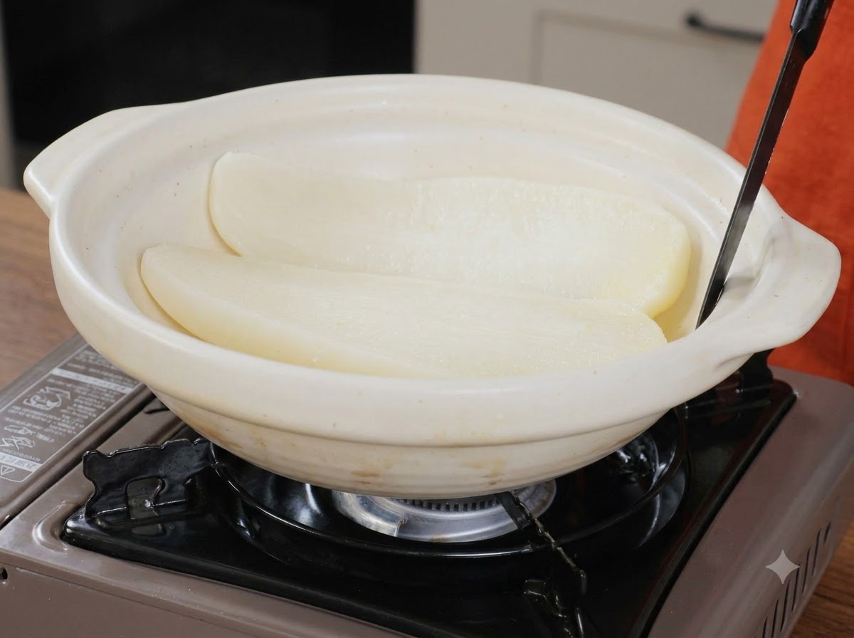 Deux moitiés de radis blanc cuit reposant à lintérieur dun grand plat de service en céramique blanche avec un ustensile.