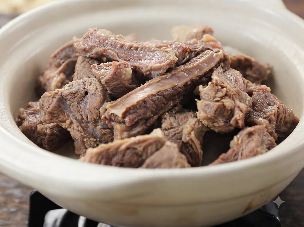 Gros plan de tendres morceaux de côtes de bœuf cuites empilés dans un plat en céramique blanche.