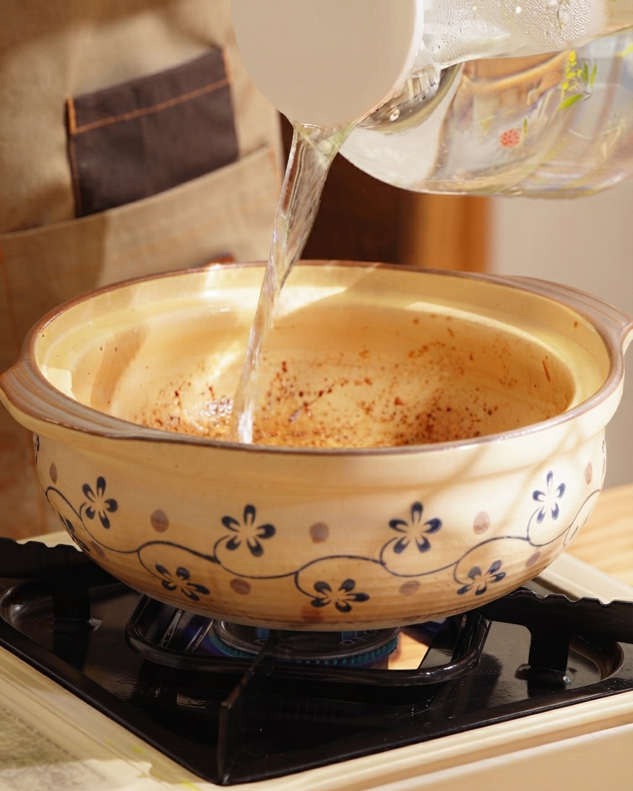 Eau chaude claire versée dune carafe dans une cocotte en argile décorée sur une cuisinière.