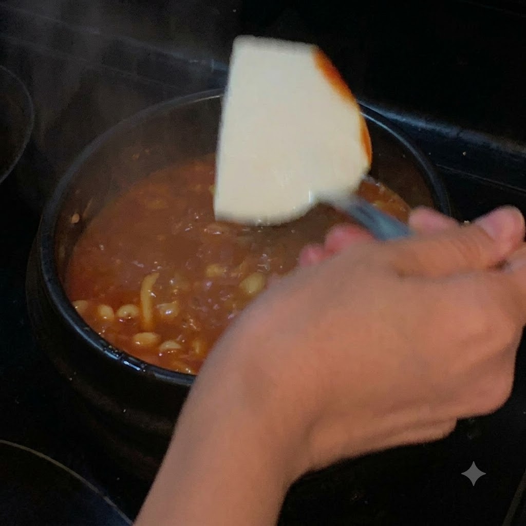 Une tranche de tofu soyeux descendue avec une spatule dans un pot de soupe rouge frémissante.