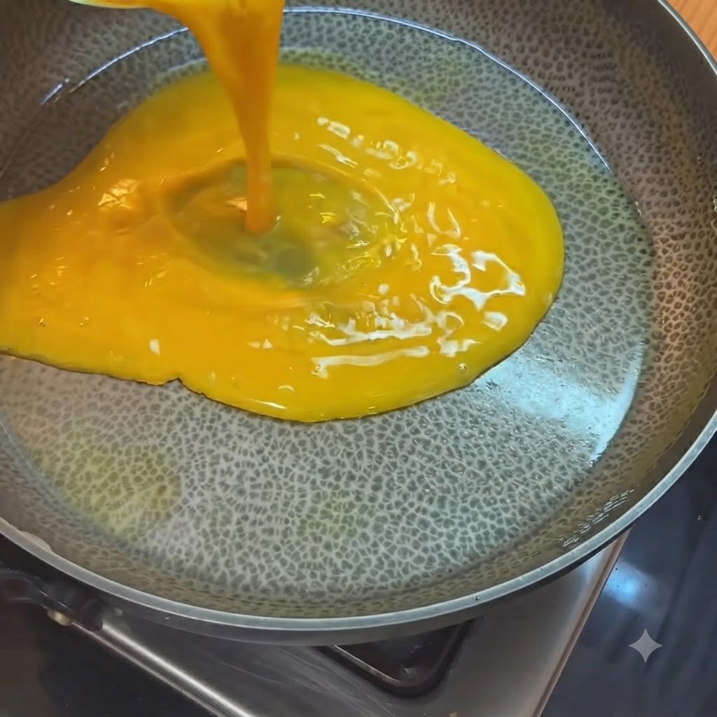 Des œufs battus jaune vif versés dun verre mesureur dans une poêle chaude huilée.