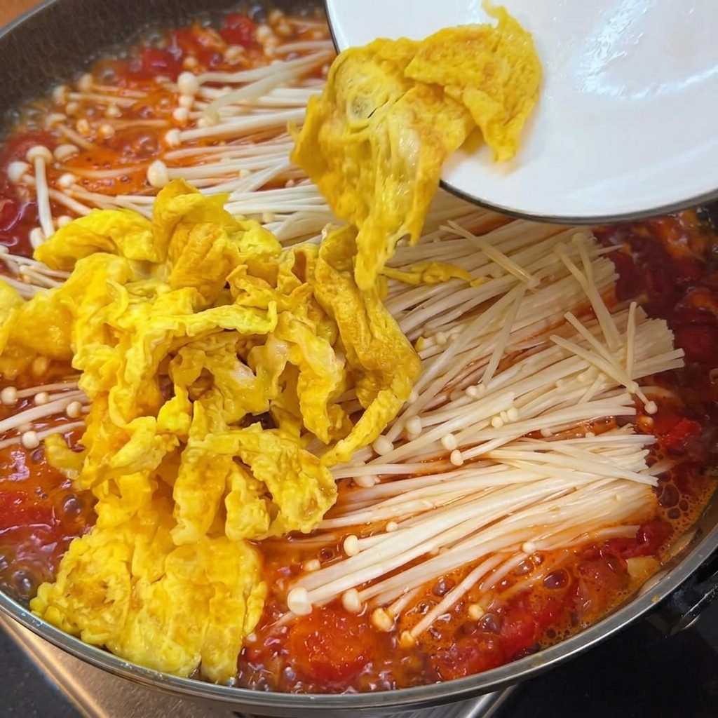 Des cubes de tofu tendre ajoutés dans la casserole contenant le bouillon de tomates, les champignons et les œufs.