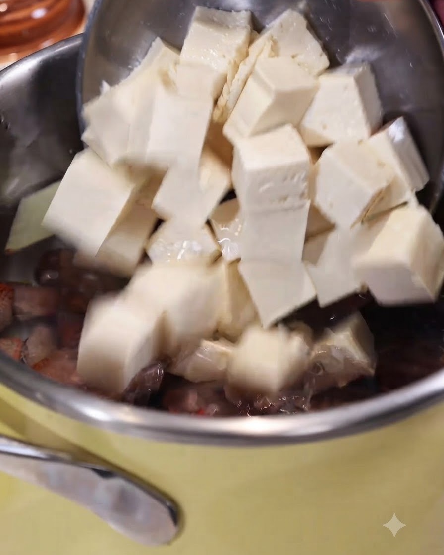 Des cubes de tofu glissant dune cuillère écumoire dans une casserole deau bouillante avec du gingembre et des palourdes.