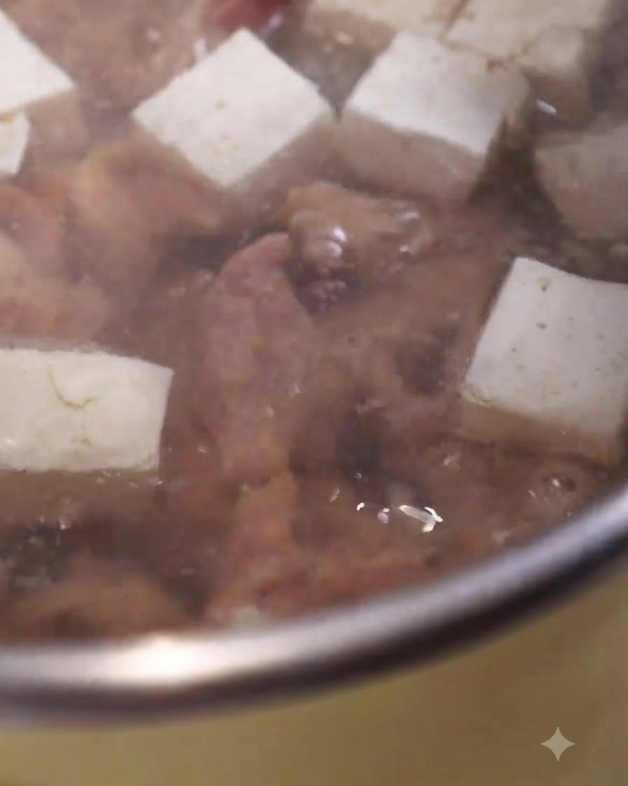 Tranches de porc mariné cuisant dans une casserole de soupe frémissante aux côtés de cubes de tofu blanc.