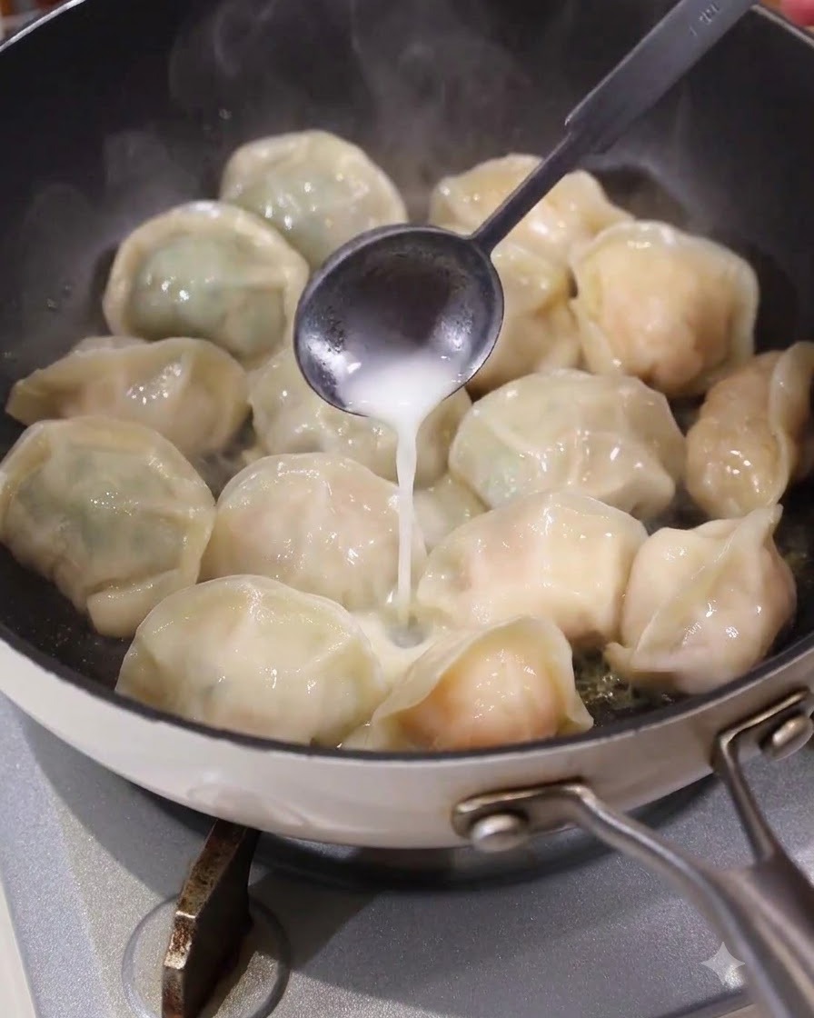 Une cuillère versant un liquide blanc de type pâte de manière homogène dans les espaces entre les raviolis dans une poêle à frire chaude.