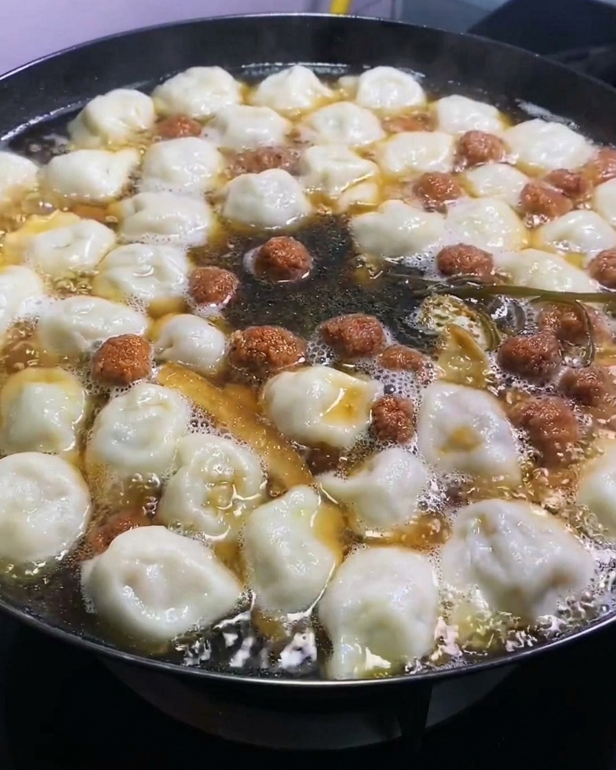 Sauce soja foncée ajoutée à une grande marmite de raviolis et dingrédients frémissants, apportant une couleur riche.