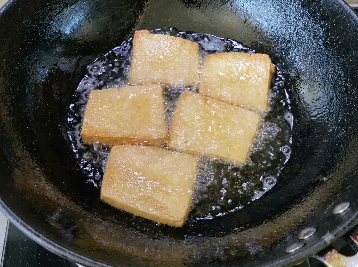 Des morceaux de tofu dorés frits dans un wok dhuile bouillante.