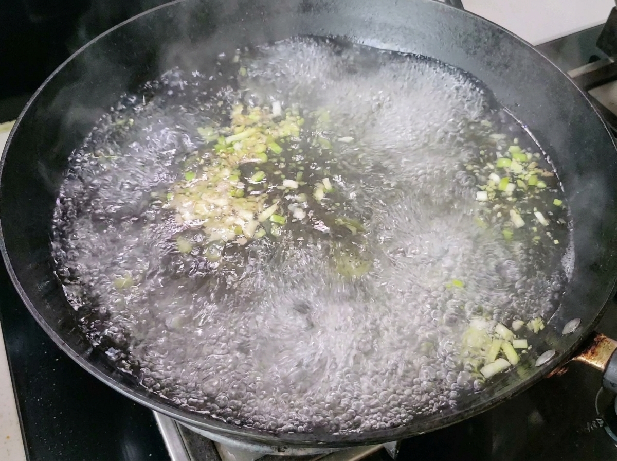 De leau bouillante avec des échalotes et du gingembre produisant de la vapeur dans le wok.