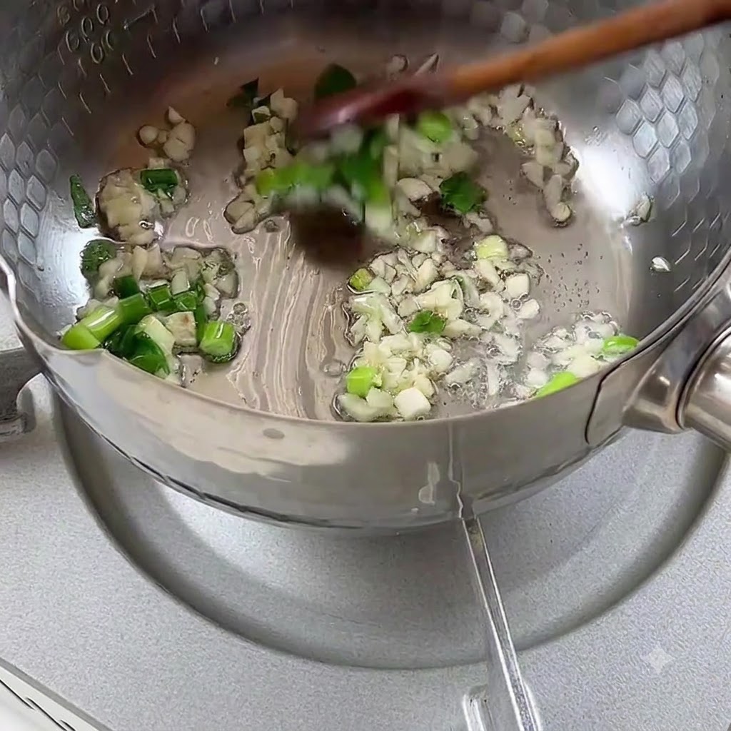 Oignons verts hachés et ail grésillant dans lhuile de cuisson à lintérieur dune casserole en métal.