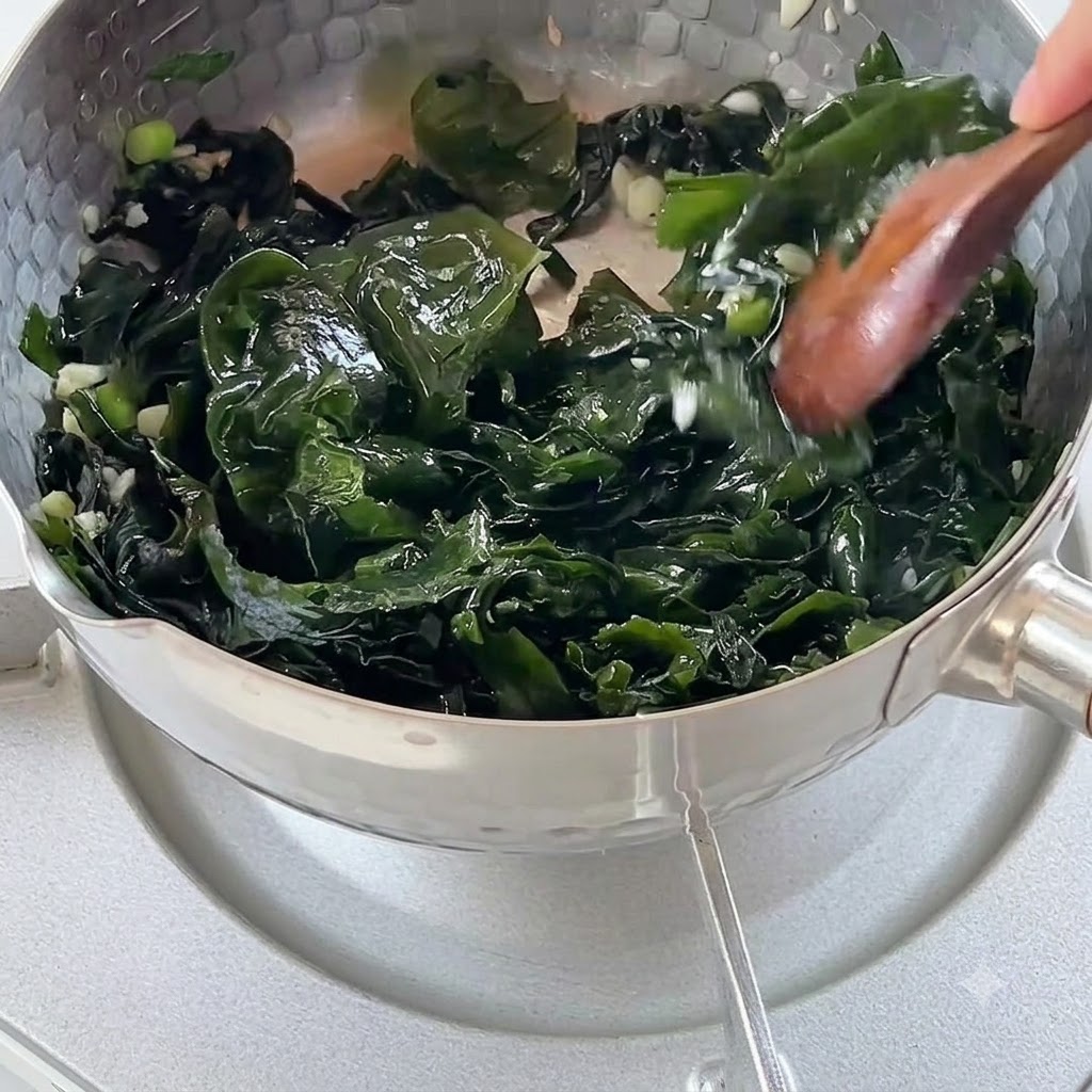 Eau bouillante versée dans une casserole remplie dalgues sautées et daromates.