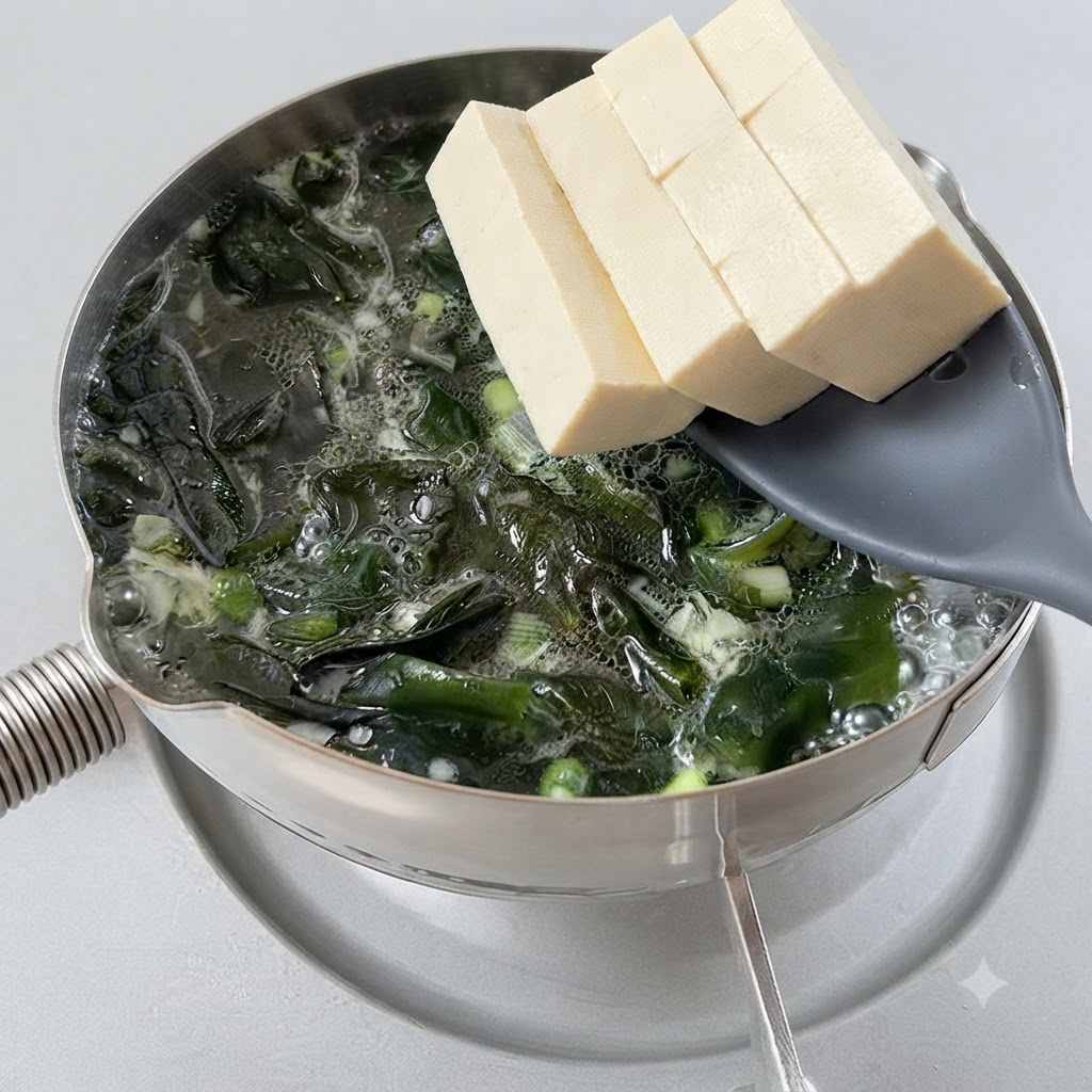 Cubes de tofu transférés dans une soupe dalgues frémissante à laide dune cuillère ajourée.
