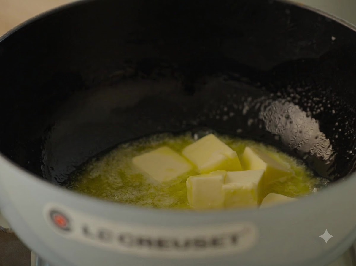 De grands morceaux de beurre doux fondant et bouillonnant dans une cocotte en fonte bleu clair.