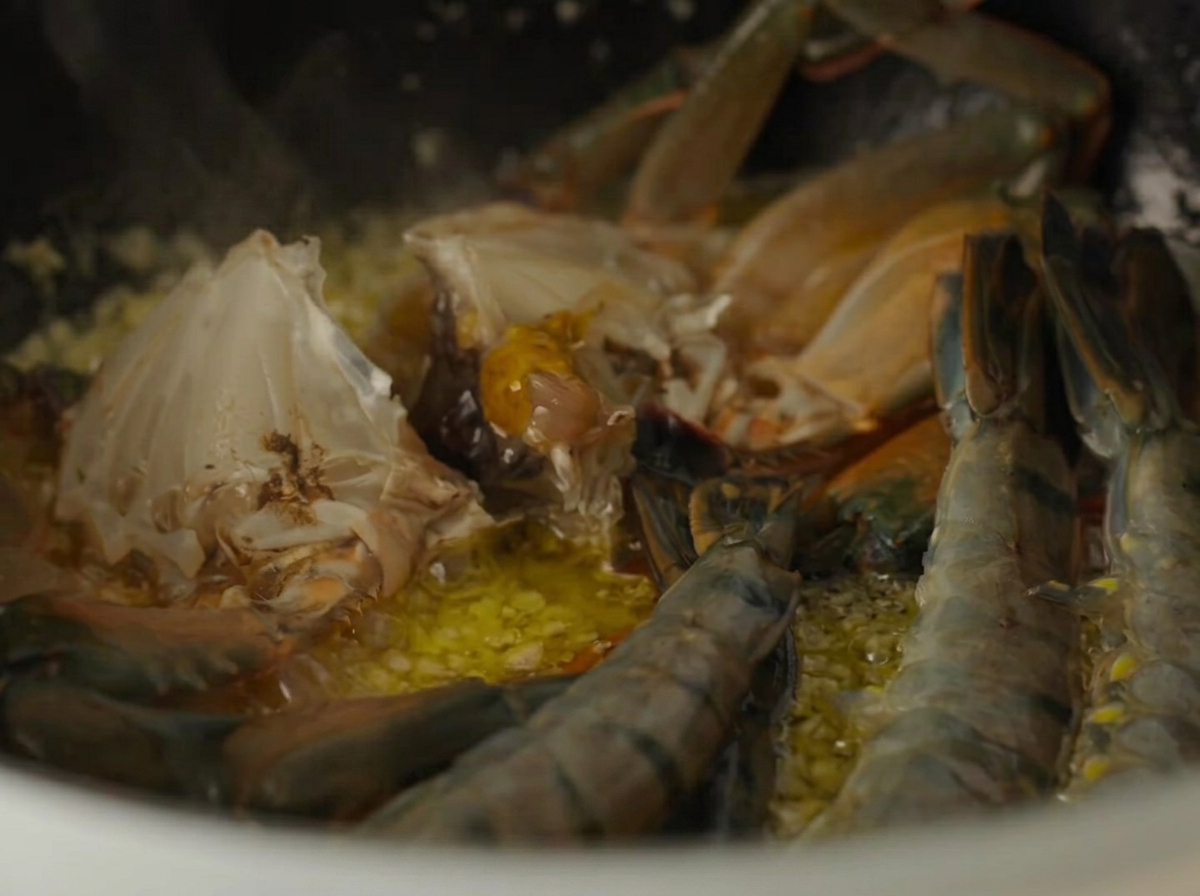 Morceaux de crabe crue et crevettes crues cuisant à lintérieur dune cocotte avec du beurre à lail.