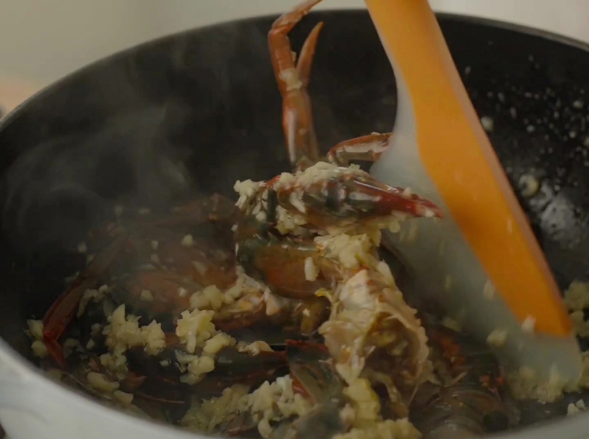 Une spatule en silicone remuant le crabe et les crevettes à lintérieur dune cocotte fumante.
