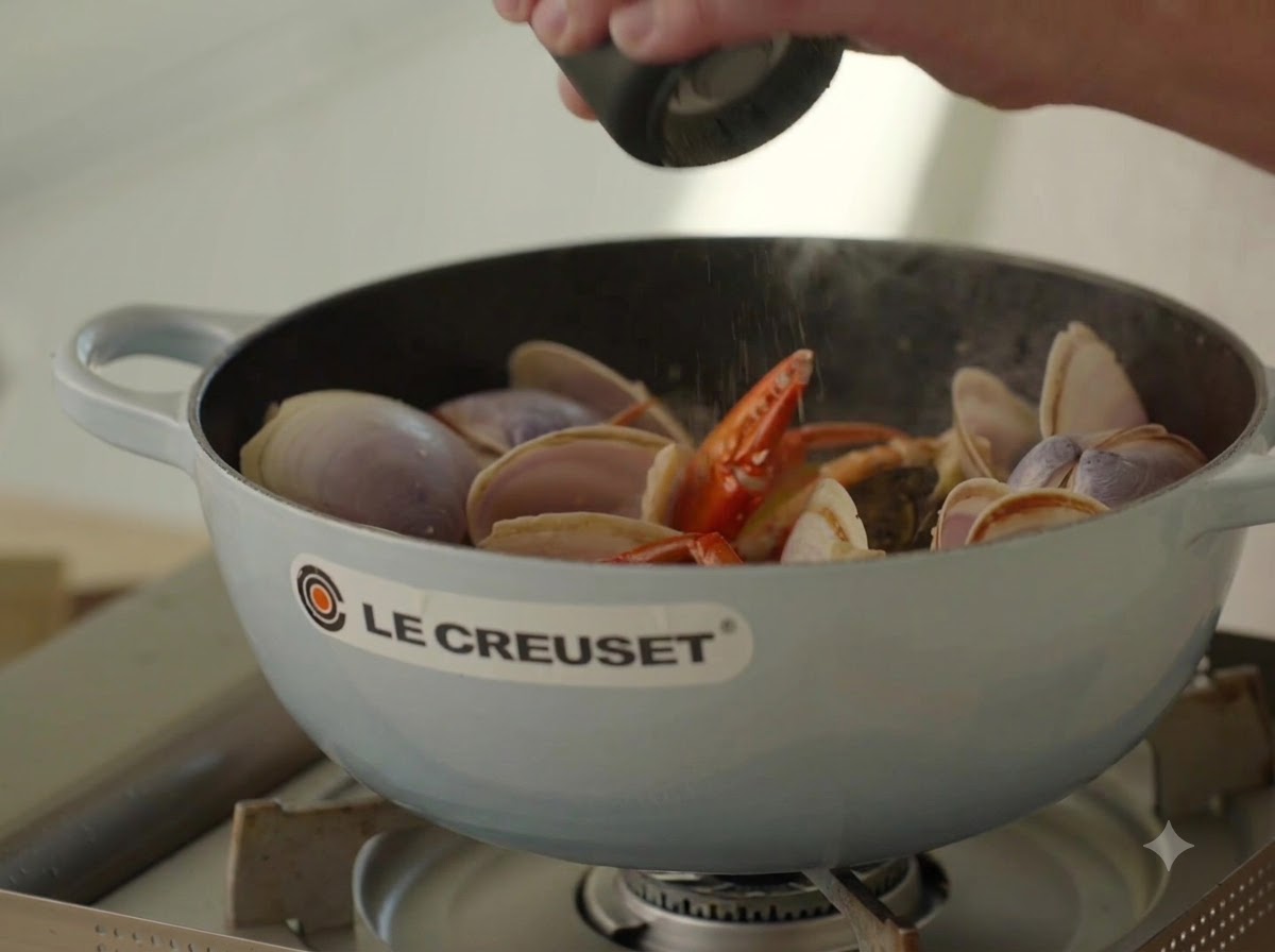 Poivre noir frais en train dêtre moulu sur un bouillon de fruits de mer bouillonnant dans une cocotte.