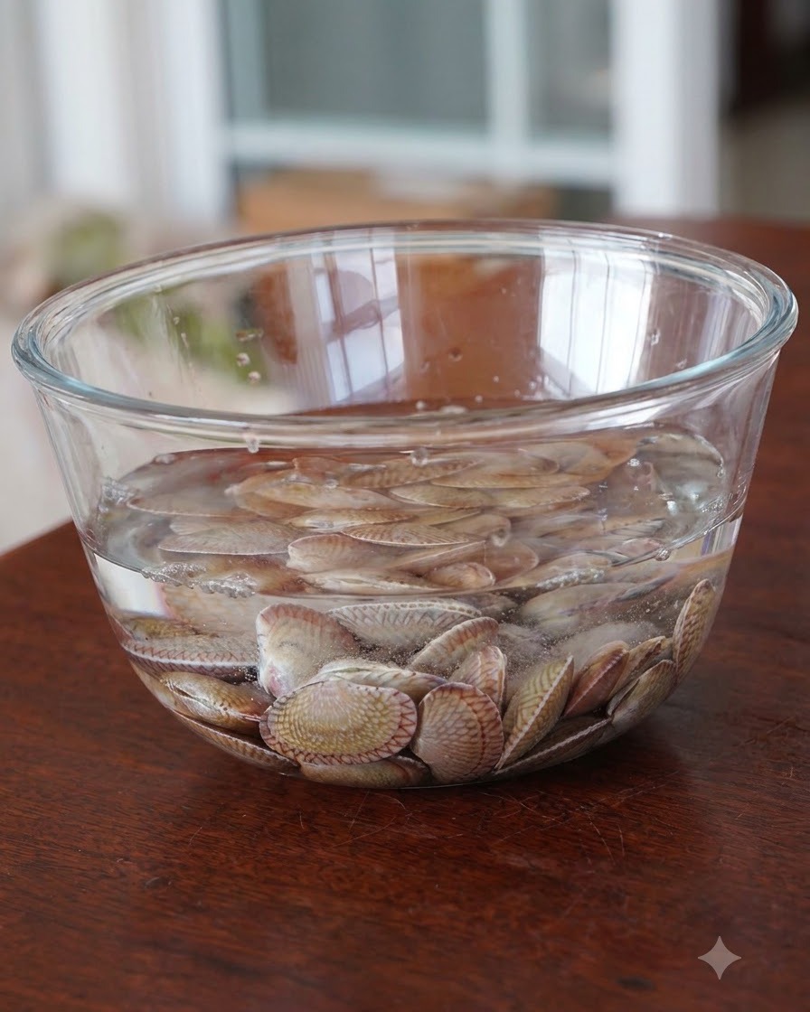 Des palourdes fraîches trempant dans un bol en verre rempli deau.