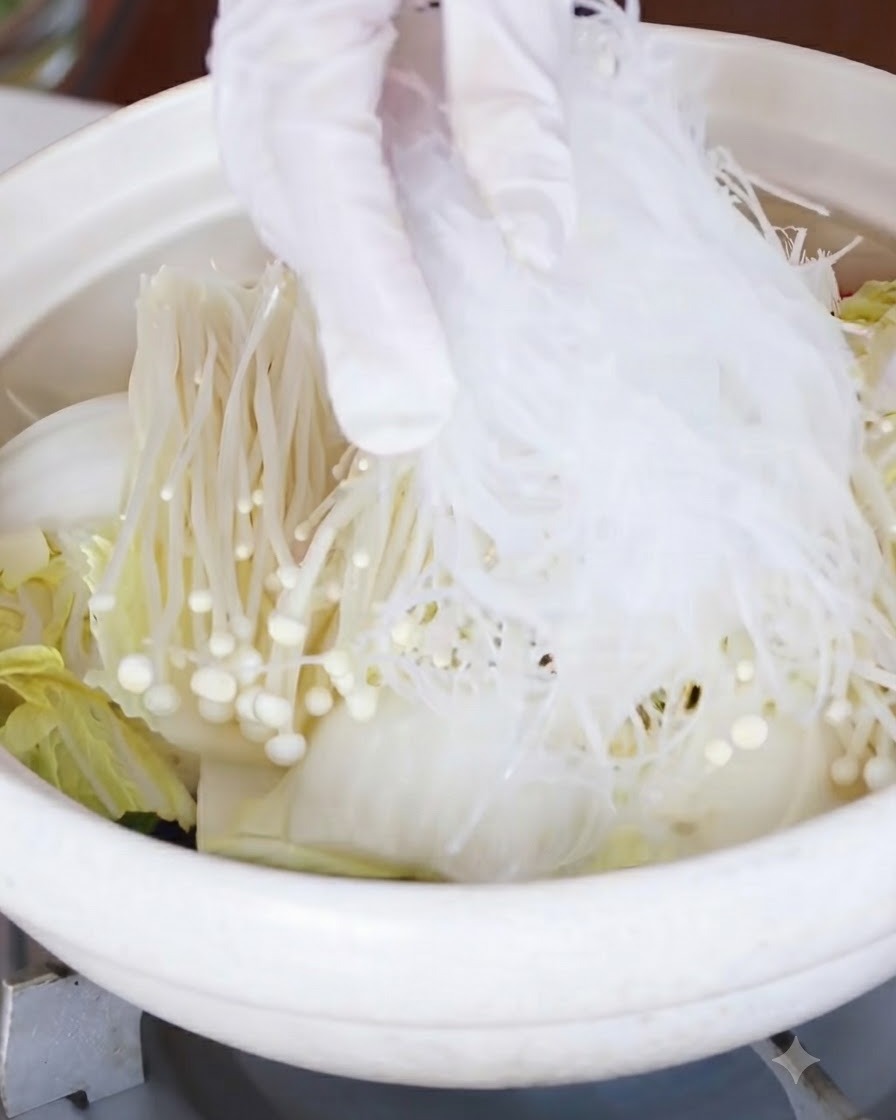 Des vermicelles ramollis placés sur la couche de champignons enoki et de chou.
