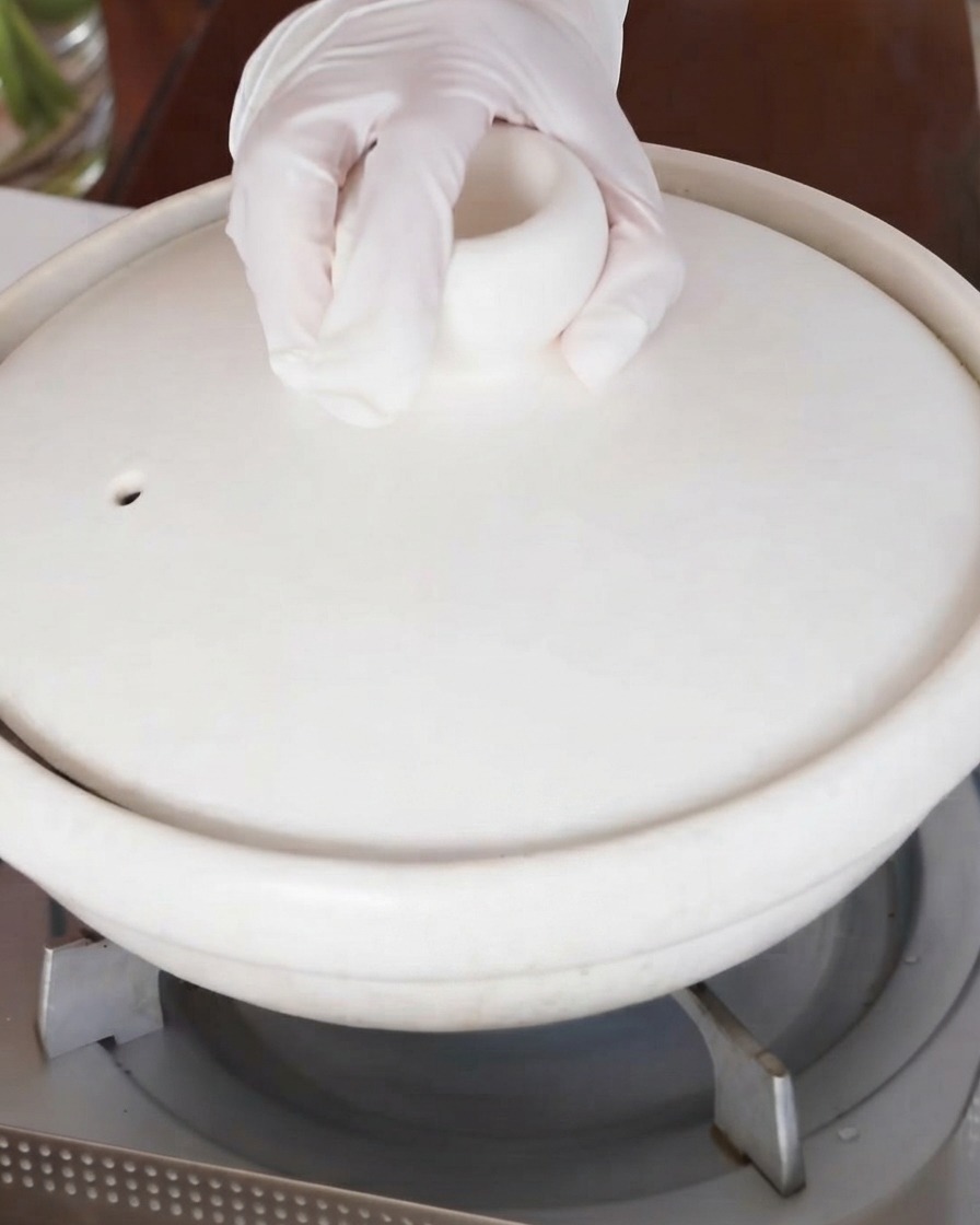 Une main plaçant le couvercle sur la marmite en céramique blanche sur la cuisinière.