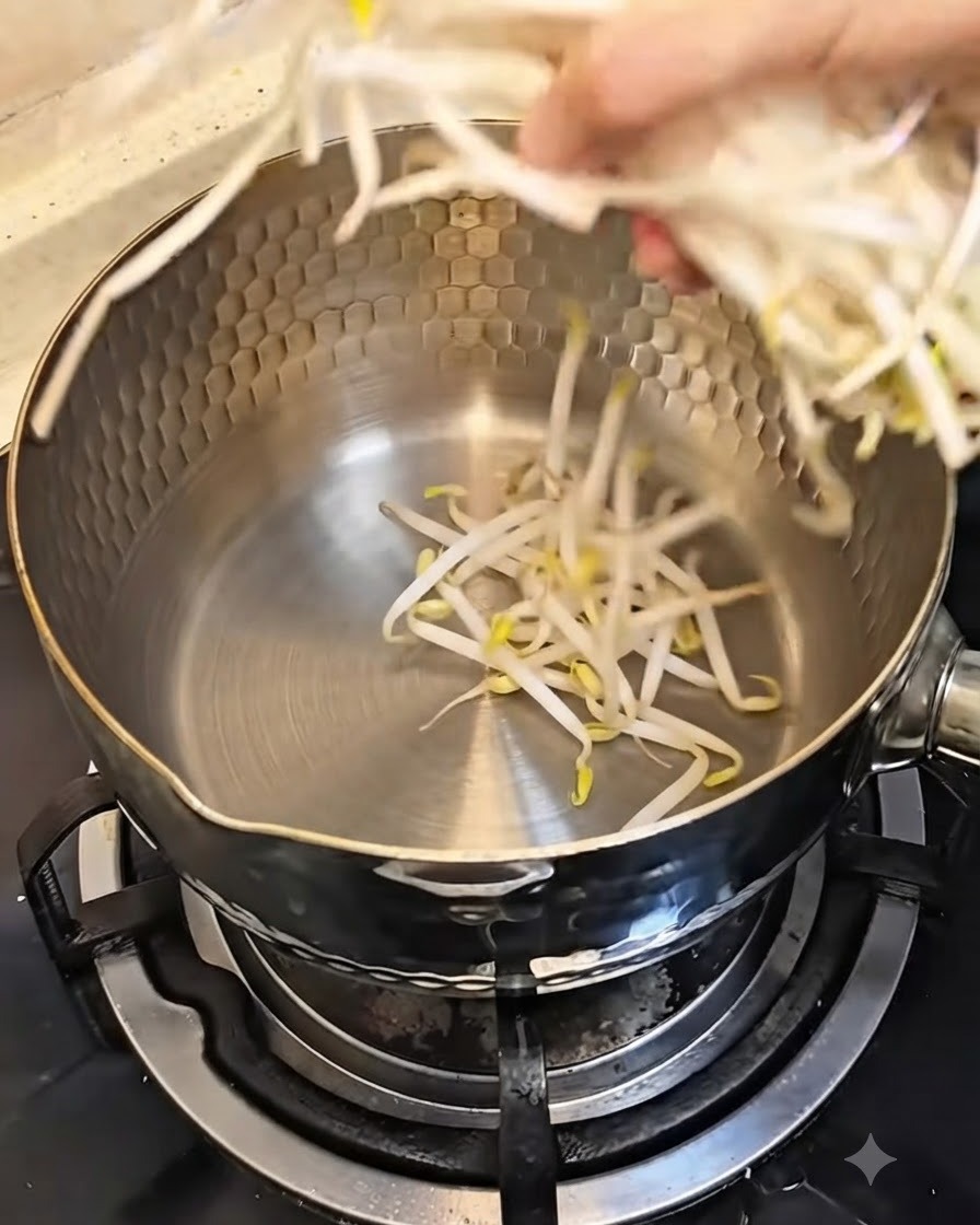 Une main plaçant une poignée de pousses de soja fraîches dans une casserole en métal propre.
