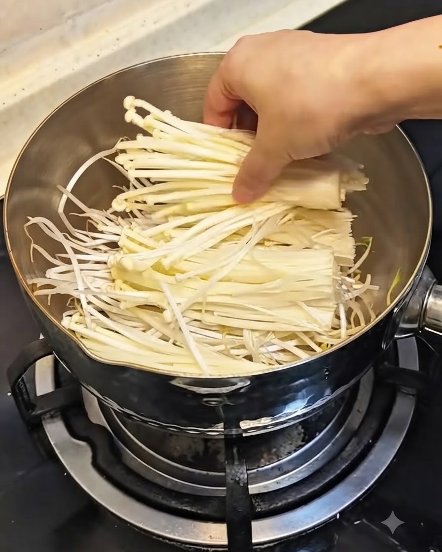 Une main plaçant une botte de champignons enoki blancs frais sur les pousses de soja dans la casserole.