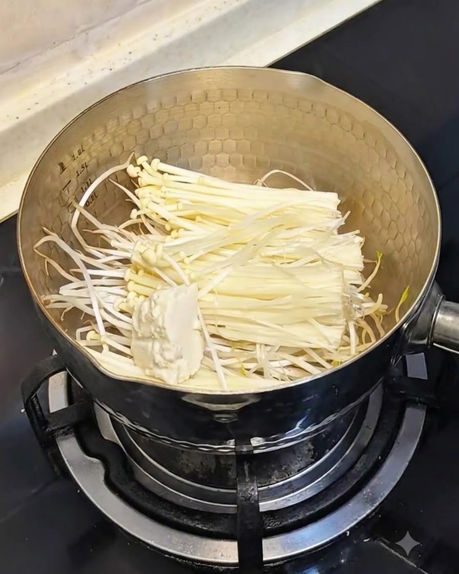 Une cuillère de tofu soyeux mou ajoutée dans la casserole contenant les pousses de soja et les champignons.