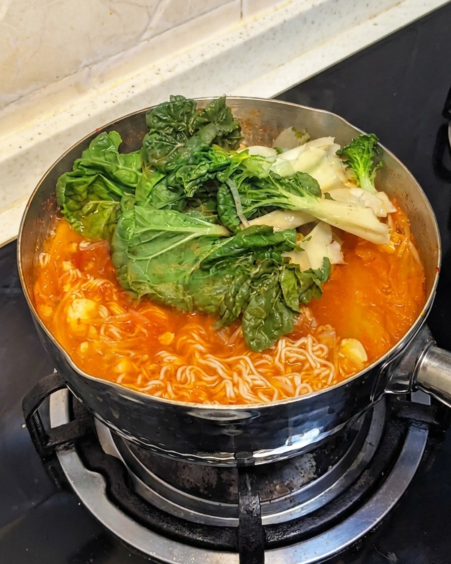 Des légumes verts à feuilles frais ajoutés par-dessus les ingrédients en ébullition dans la casserole.