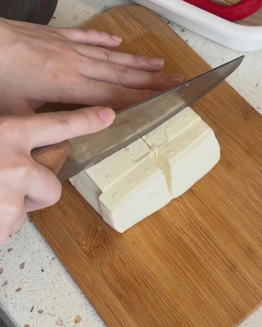 Un bloc de tofu blanc découpé en petits morceaux rectangulaires sur une planche en bois.