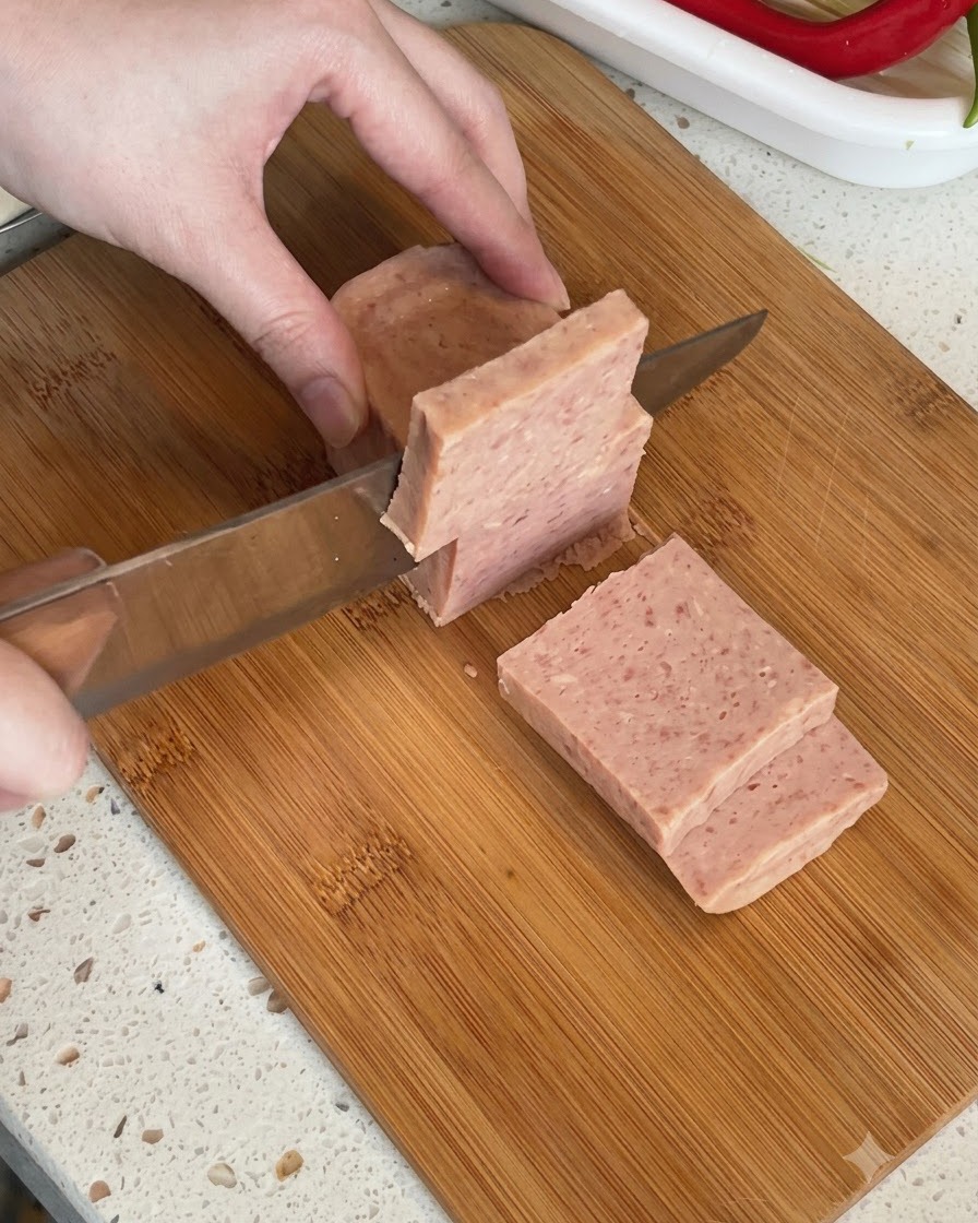 Un bloc de viande de luncheon en conserve tranché en morceaux épais sur une planche à découper.