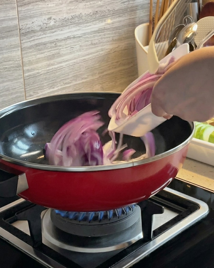 Des tranches doignon rouge en train dêtre sautées dans une casserole rouge sur un brûleur à gaz.