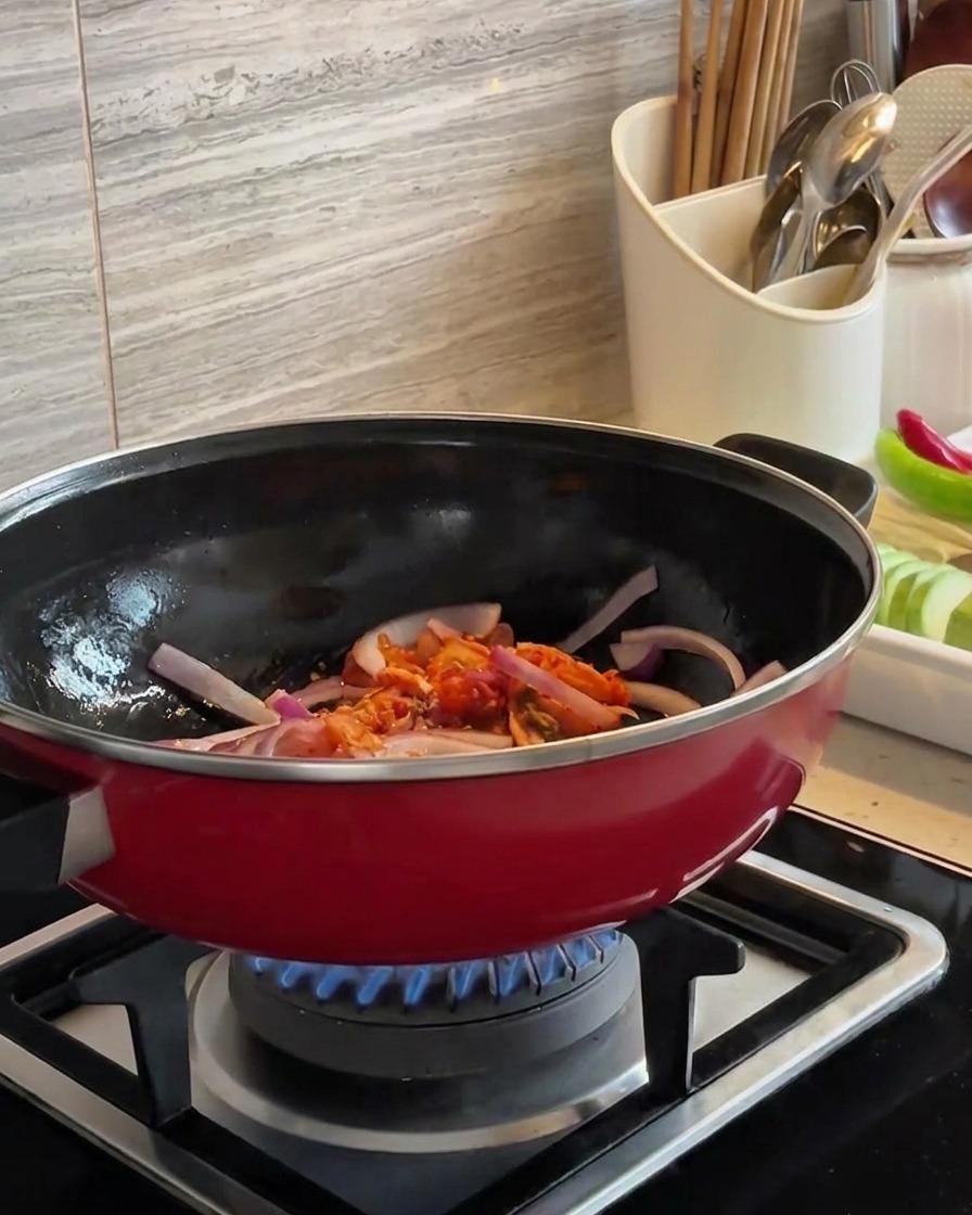 Des tranches doignon rouge et du kimchi haché sautés ensemble dans un wok rouge au-dessus dune flamme bleue.