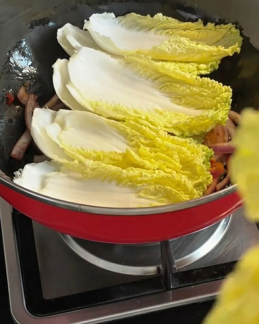 Des feuilles de chou chinois frais disposées en couches sur le mélange doignons et de kimchi sautés.