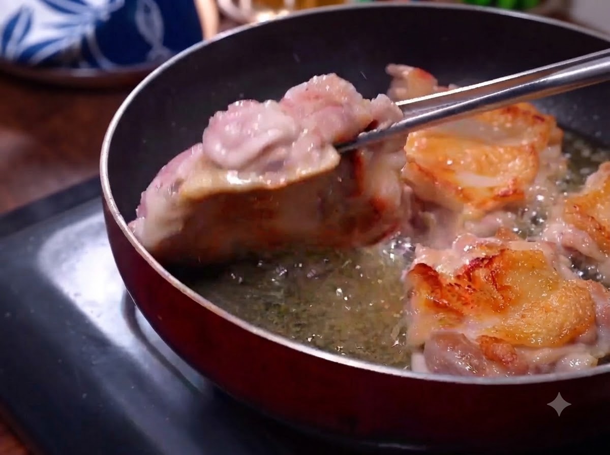 Cuisses de poulet en train de frire dans une poêle avec une peau dorée visible tandis que des pinces les retournent.