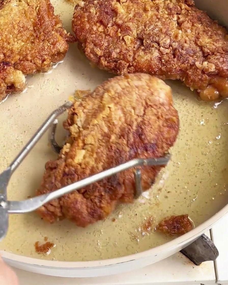 Côtes de poulet frites croustillantes soulevées hors dune poêle huileuse à laide de pinces en acier inoxydable.