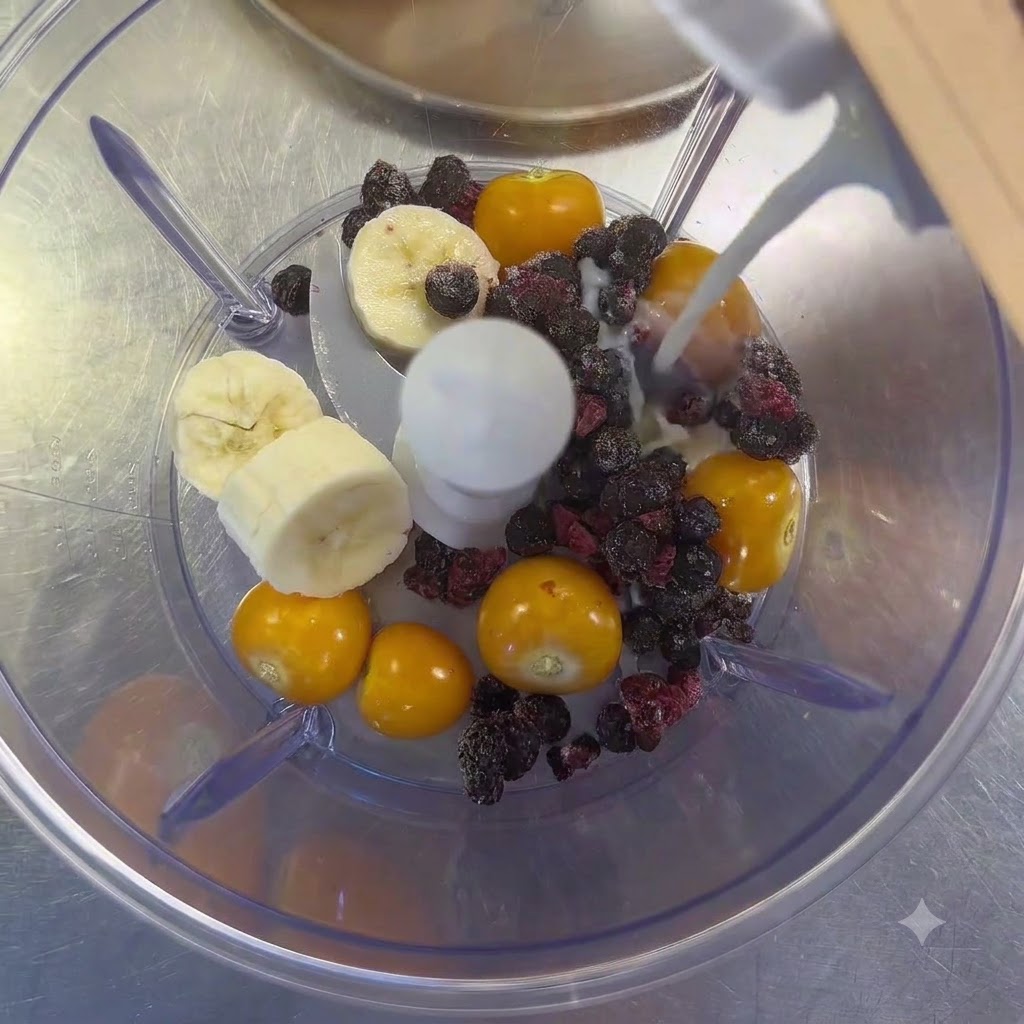 Du lait versé dune brique dans un mixeur rempli de groseilles à maquereau, de morceaux de banane et de fruits rouges.
