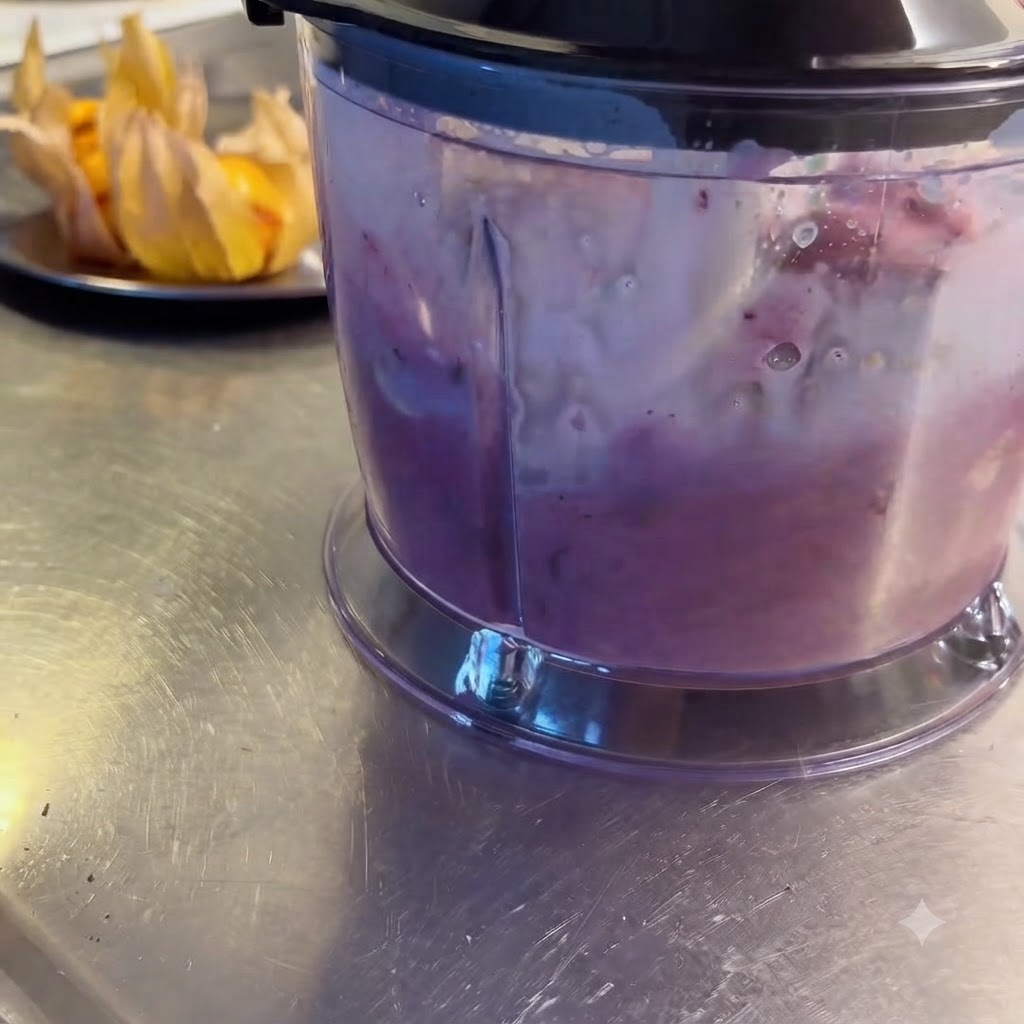 Un mixeur en train de réduire des fruits rouges et du lait en un milk-shake violet et onctueux.