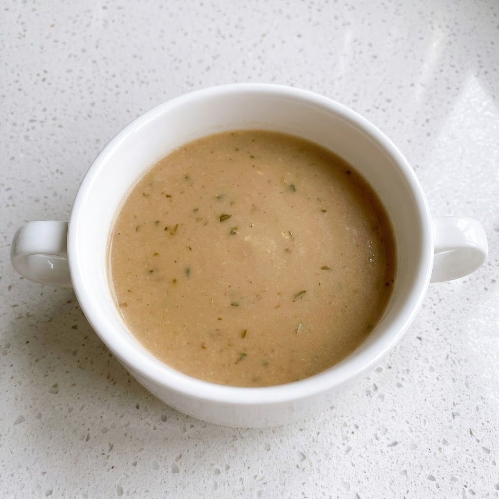 Un bol blanc contenant un mélange de sauce brune parsemé de points de poivre.