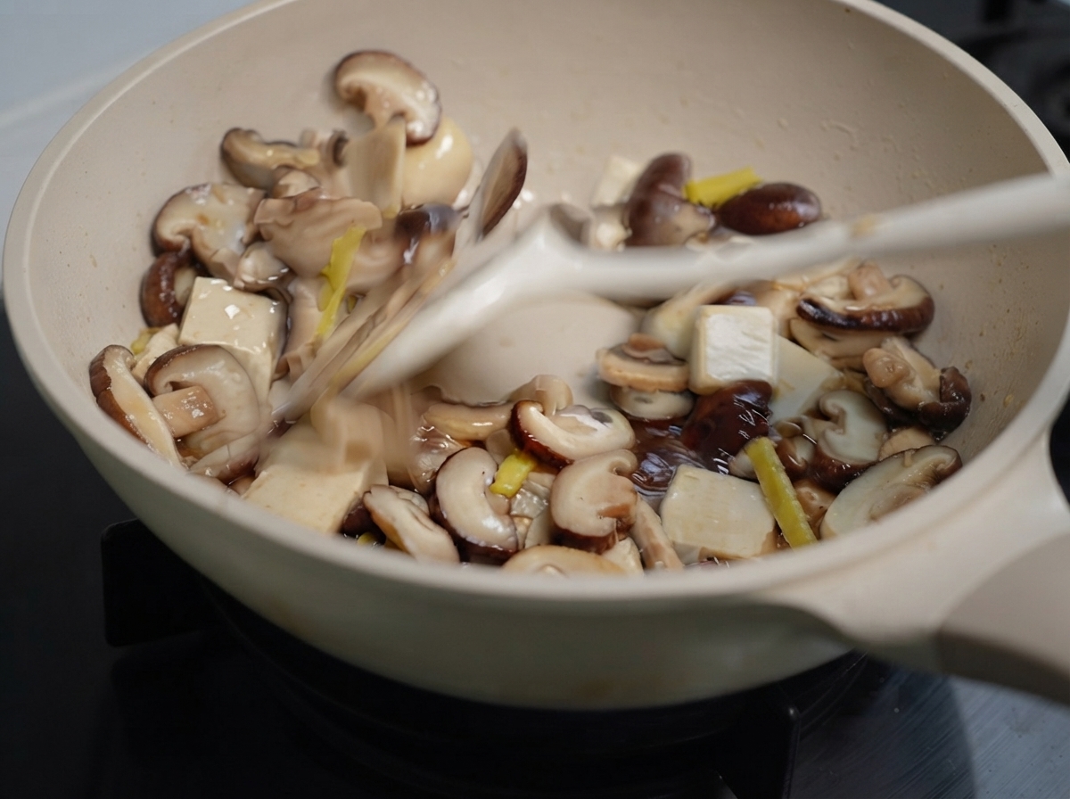 Des champignons mélangés et du gingembre en train dêtre sautés dans une poêle à laide dune spatule.