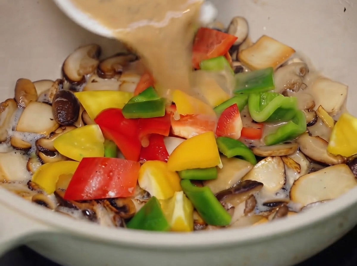 La sauce au poivre noir versée dun petit bol blanc dans la poêle contenant les champignons mélangés et les poivrons colorés.