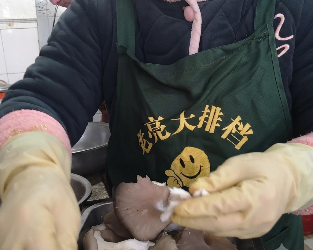 Mains portant des gants de protection jaunes déchirant des pleurotes frais en lanières individuelles.