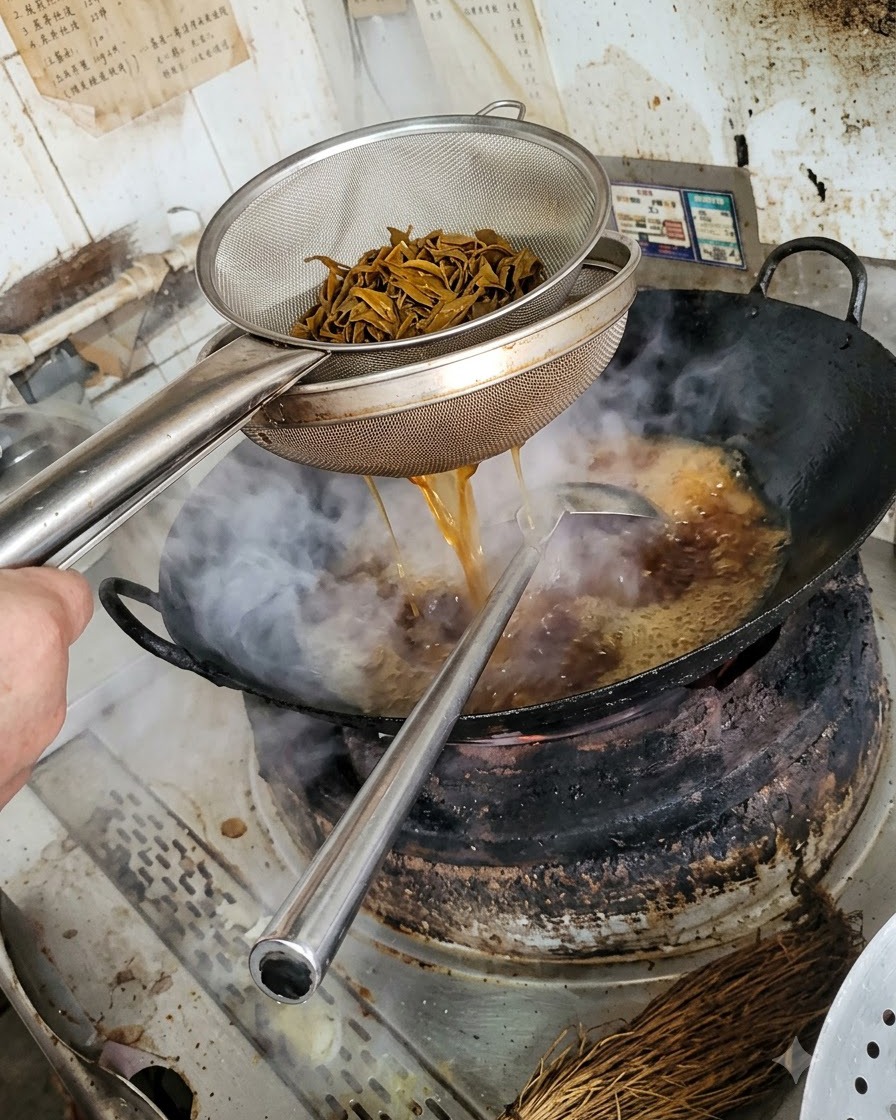 Une colandre en métal contenant des lanières de champignons foncées et blanchies, avec du liquide sécoulant dans le wok en dessous.