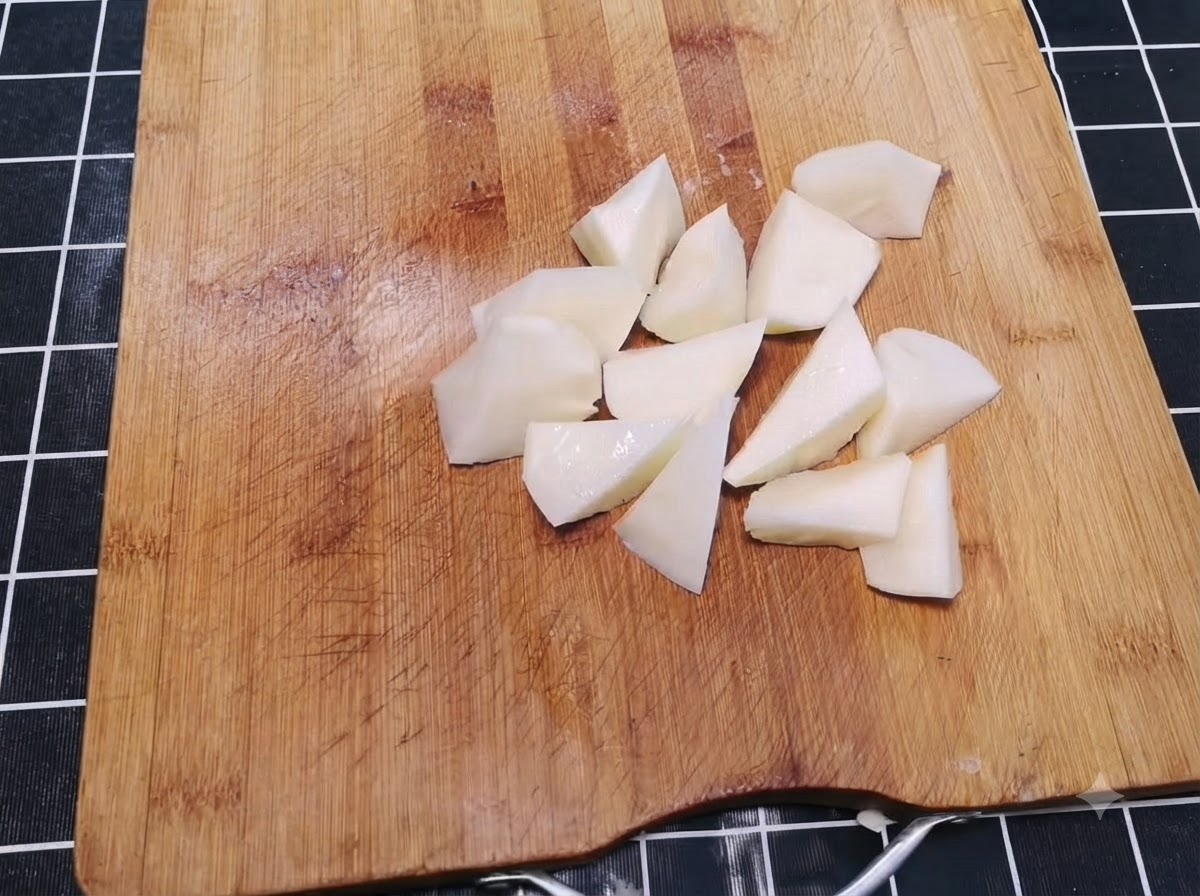 Des pommes de terre épluchées coupées en morceaux irréguliers de taille bouchée éparpillés sur une planche à découper en bois.