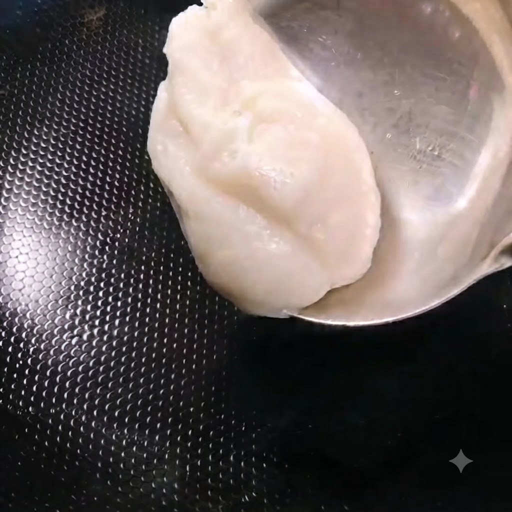 Une louche ajoutant une portion de saindoux blanc dans un wok noir chauffé.