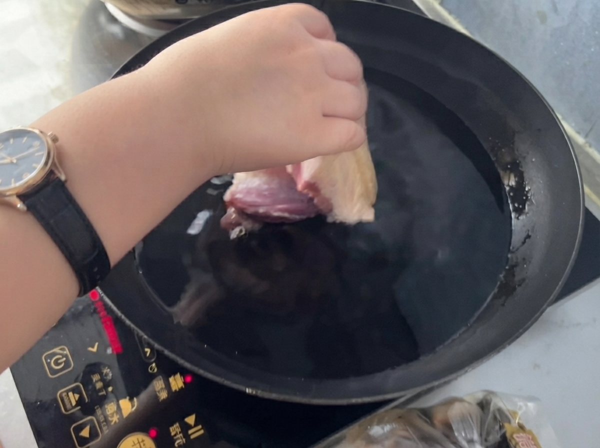 Une main plaçant un morceau de porc dans une casserole deau froide avec du gingembre et du vin de cuisine.