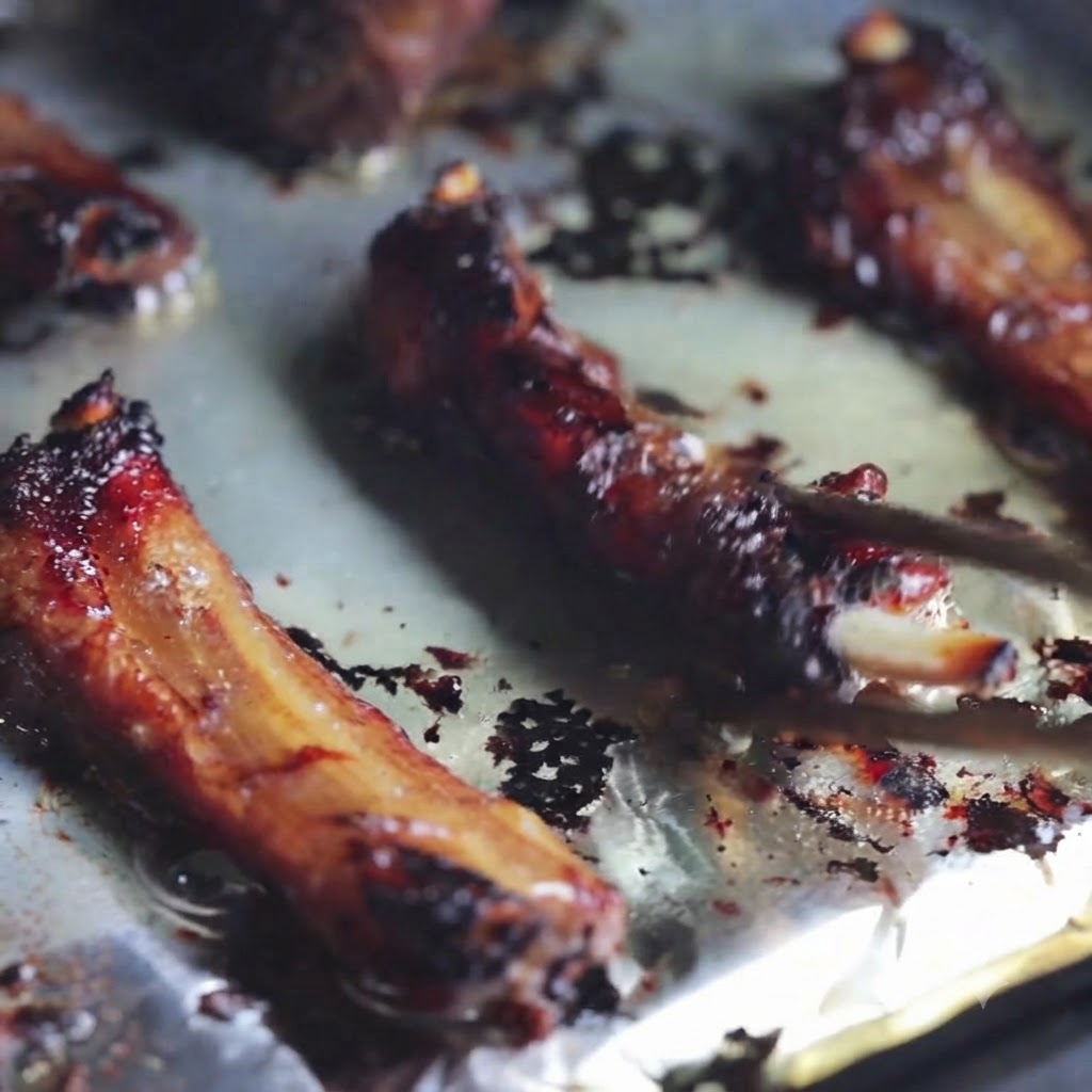 Gros plan de travers de porc grillés retournés sur une plaque de cuisson recouverte de papier sulfurisé à laide de baguettes.