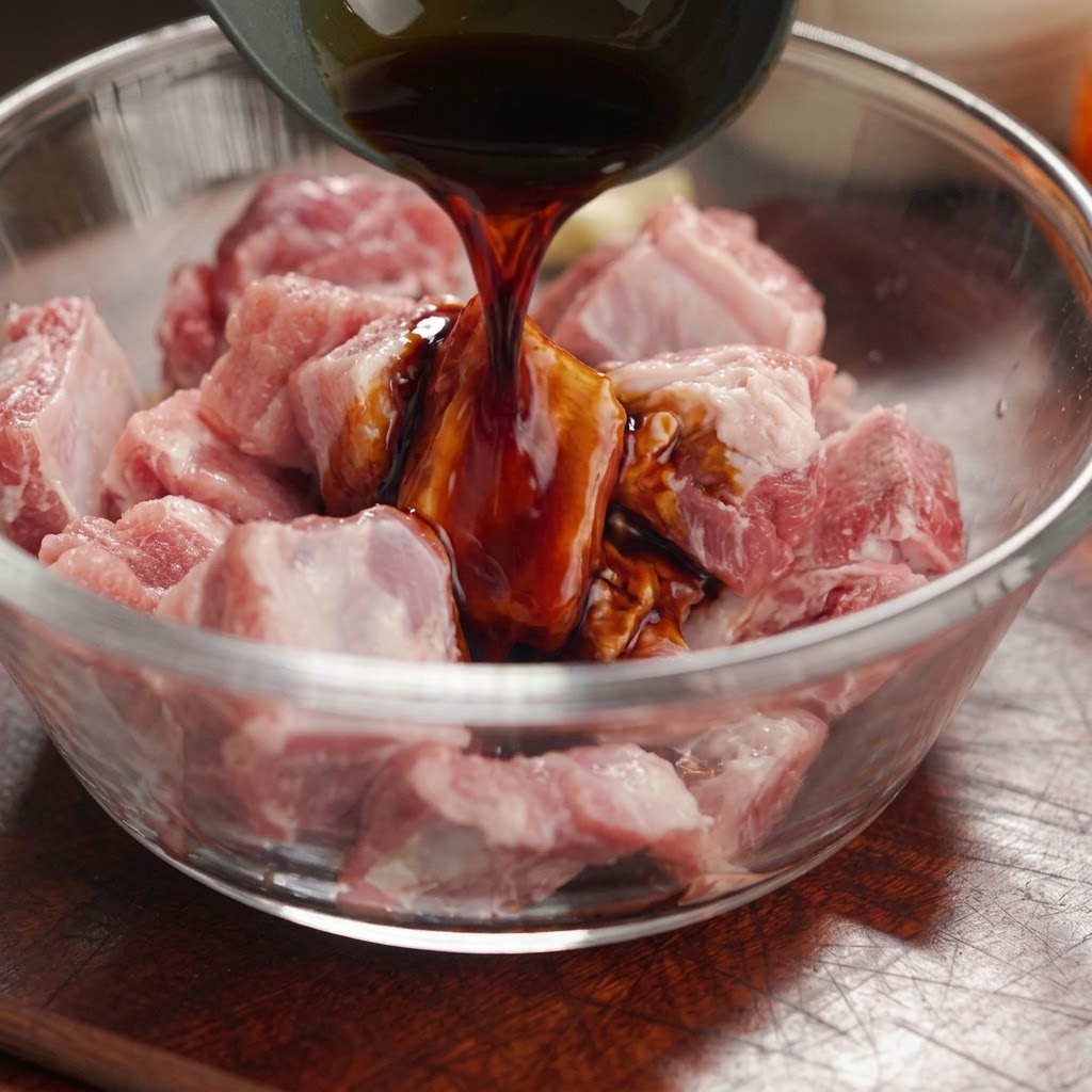 Sauce soja noire versée dune louche sur des morceaux de travers de porc crus dans un bol en verre.